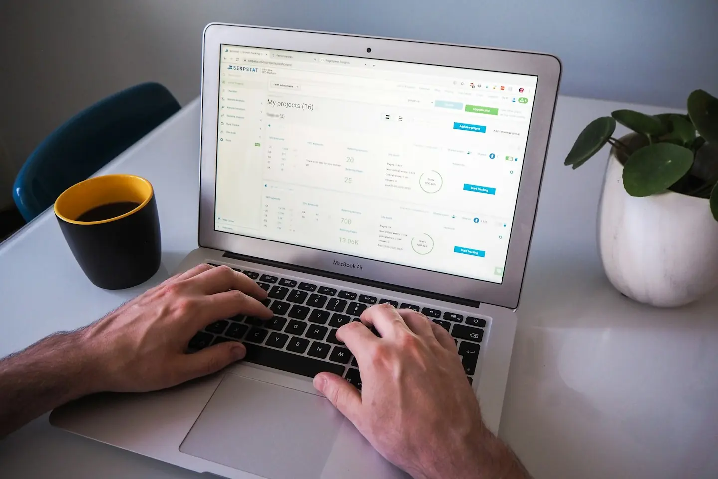 Mains sur le clavier d’un ordinateur portable, avec une tasse de café et une plante sur la table