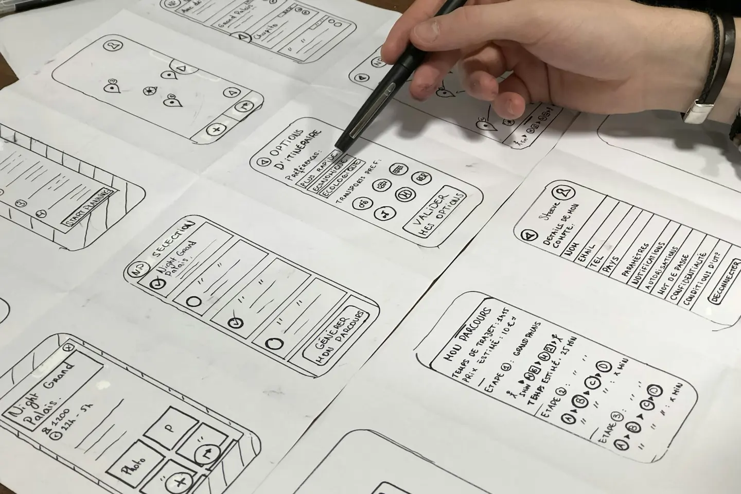Une main annote au stylo des croquis de pages d’application sur une feuille