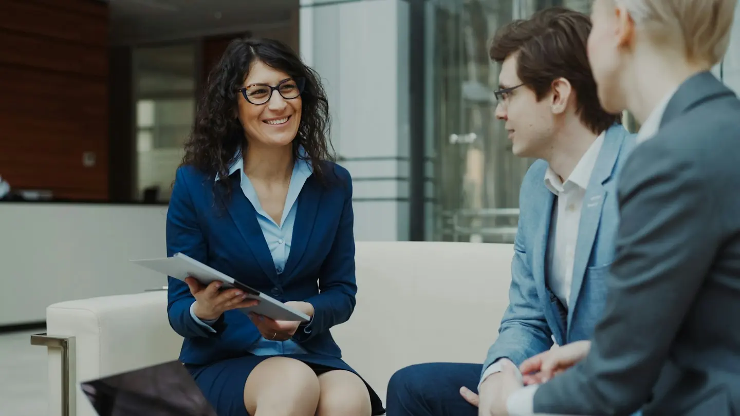 Trois collaborateurs échangent lors d’un rendez-vous client dans un salon de bureau