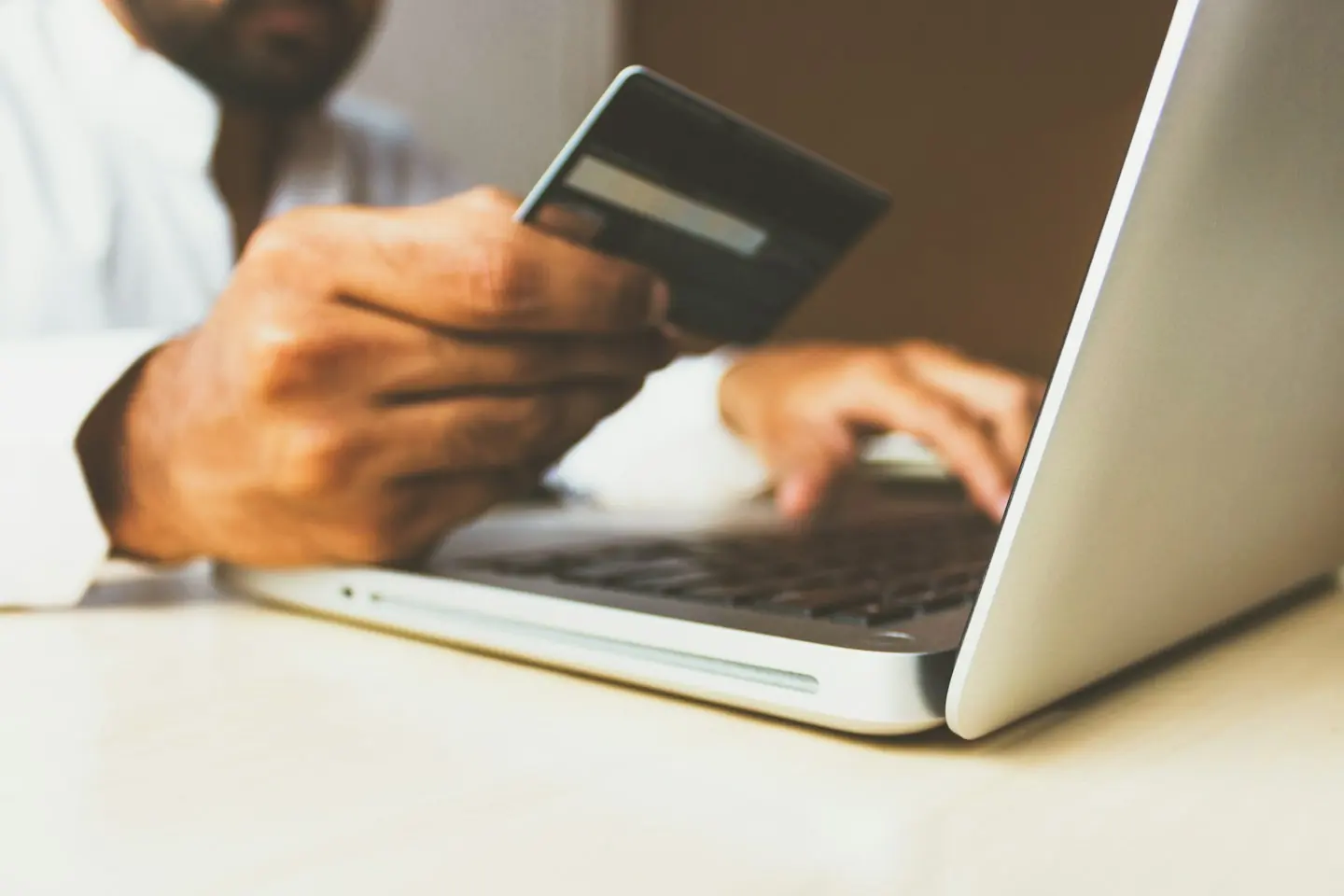Une personne tient une carte bancaire au-dessus d’un ordinateur portable pour payer en ligne