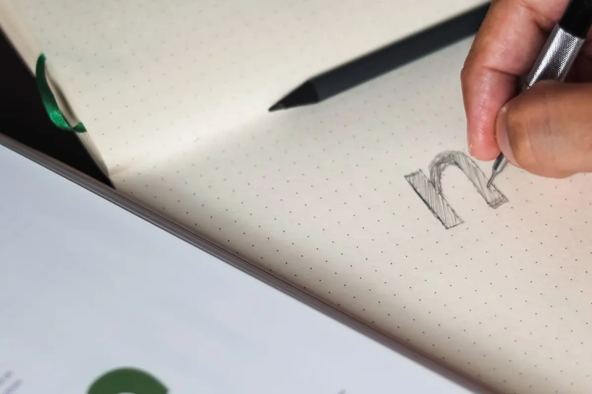 Gros plan sur une main qui dessine une lettre hachurée dans un carnet à points